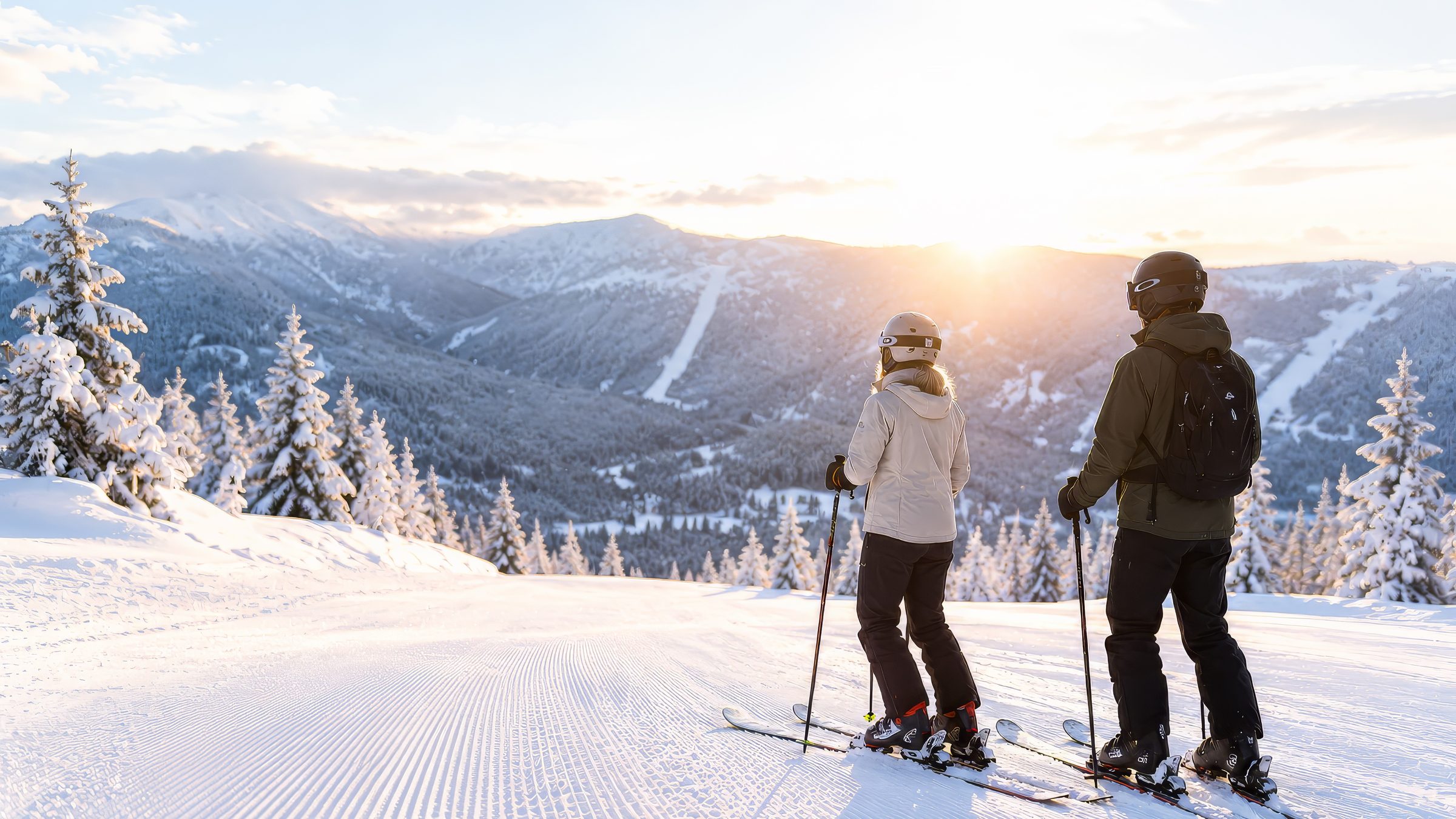Zwei Skifahrer blicken von der präparierten Piste auf die tief stehende Sonne